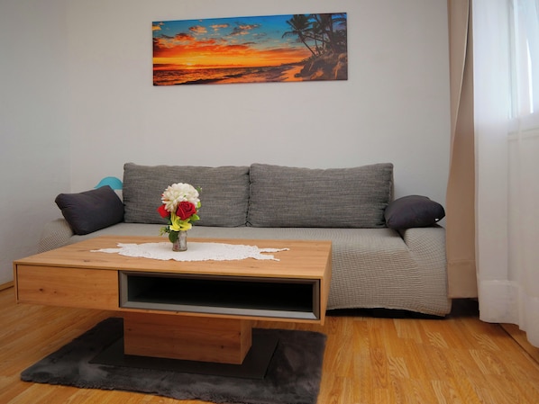 Een woonkamer met een grijze bank, een houten salontafel en een schilderij van een zonsondergang.