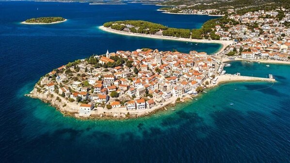 An aerial view of a coastal town with a central island featuring white buildings with red roofs, surrounded by clear blue waters and smaller islands. - Apartment Nikica (Primosten)