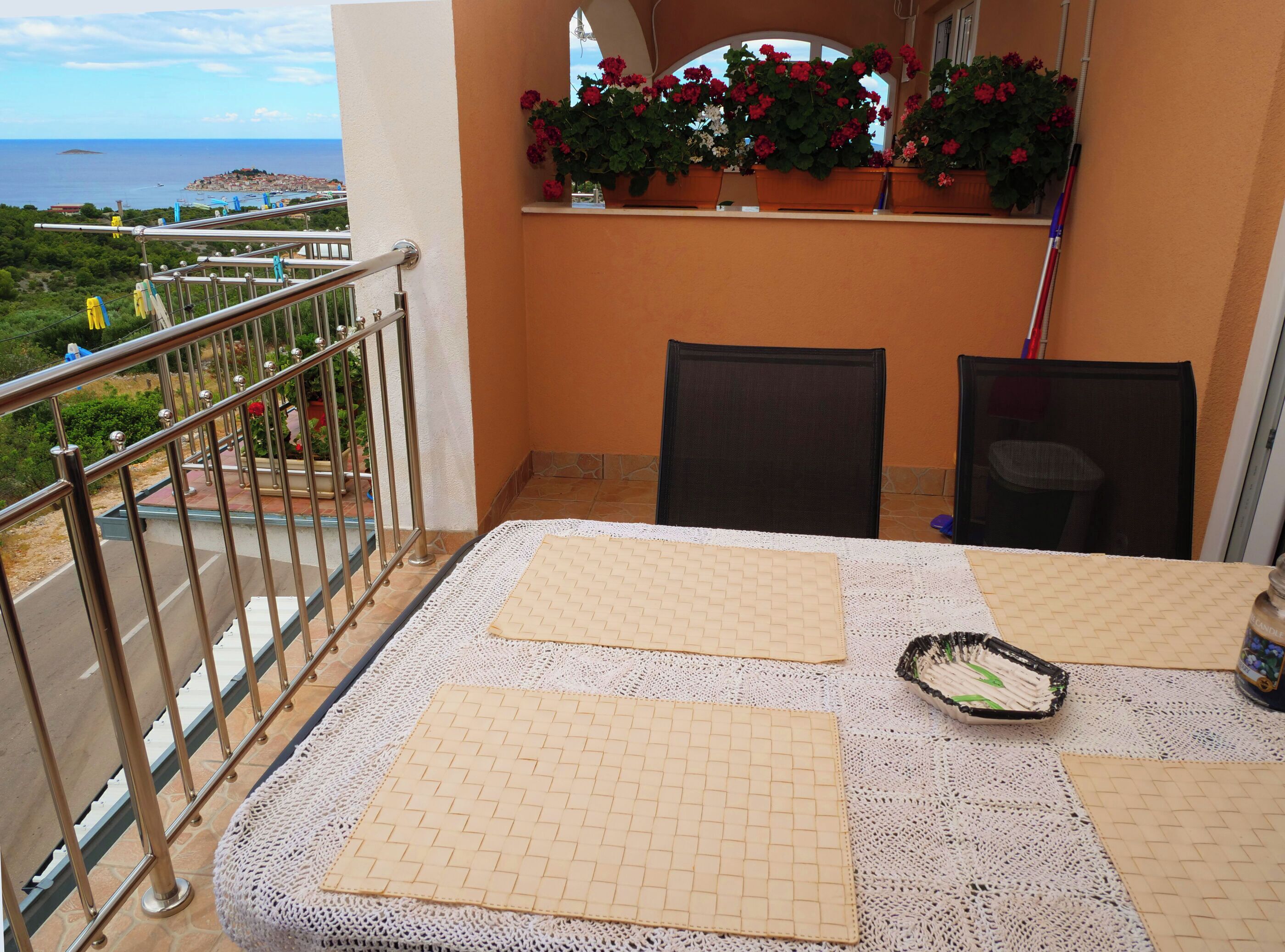 A balcony with a table set with placemats and a candle, overlooking a scenic view of the sea and a distant island.