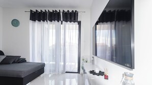 Ein modernes Schlafzimmer mit einem Bett, einem großen Fenster mit durchsichtigen Vorhängen, einem Nachttisch mit Lampe und einer Wanduhr.