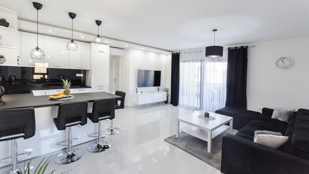 Eine moderne Wohnung mit Küche, Essbereich und Wohnzimmer. Sie verfügt über eine große Kochinsel mit Barhocker, einen Flachbildfernseher und einen Couchtisch.