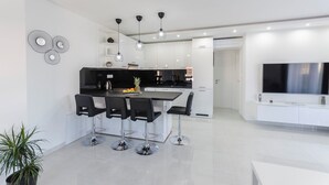 Eine moderne Küche mit einer zentralen Kochinsel, schwarzen Barhocker, Pendelleuchten und einem großen Flachbildfernseher.