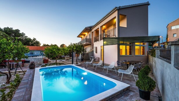 A rectangular swimming pool with a tiled deck, surrounded by lounge chairs and a covered seating area.