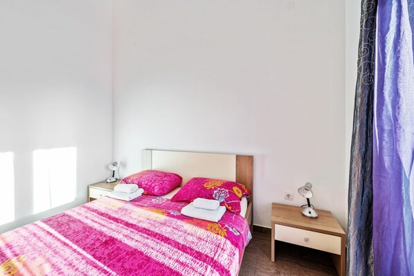 A bed with a pink and white striped bedspread, two pillows, and a nightstand with a lamp. - House Jakov (Rogoznica)