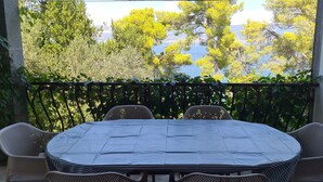 A balcony with a table and chairs, overlooking a body of water and trees. - Apartment Iskra (Split)