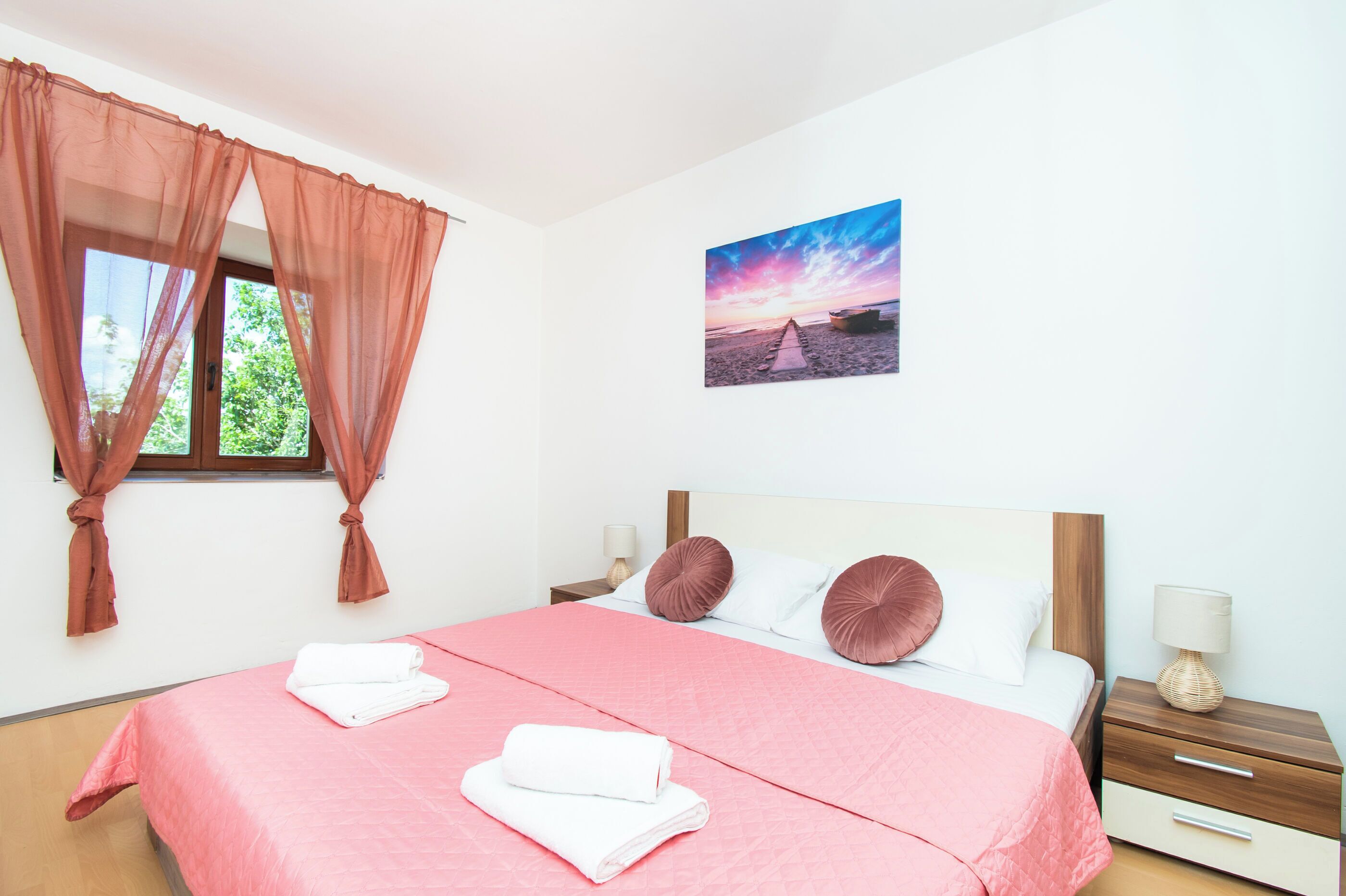A bedroom with a bed, a nightstand, a window with curtains, and a wall-mounted picture.