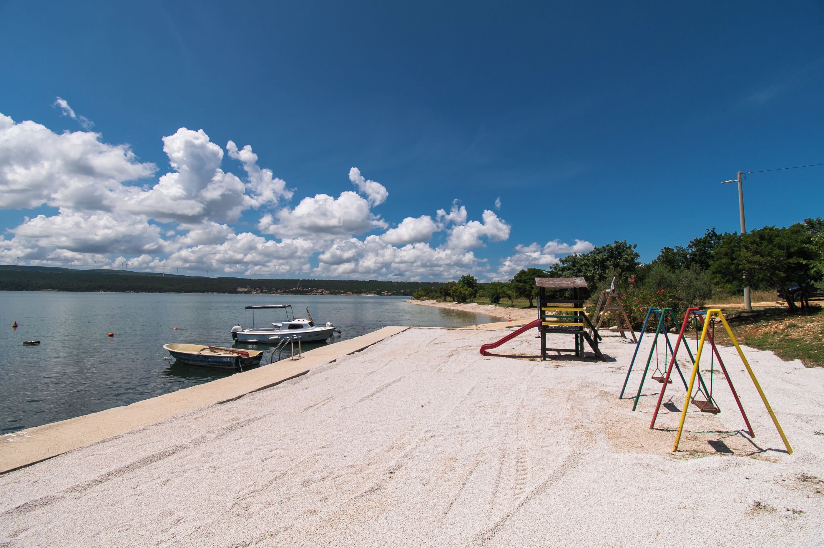 A sandy beach with a swing set and a row of boats docked near the water.