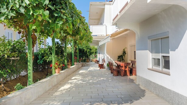A paved outdoor corridor with potted plants and outdoor furniture, leading to a building entrance. - Apartments Ruza A (Lopar)