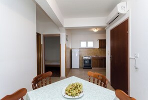 A dining area with a table set for two, a kitchen in the background, and a door leading to another room. - Apartments Ruza A (Lopar)