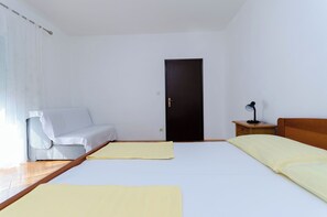 A room with two beds, a sofa, a wooden nightstand, a door, and a window with curtains. - Apartments Ruza A (Lopar)