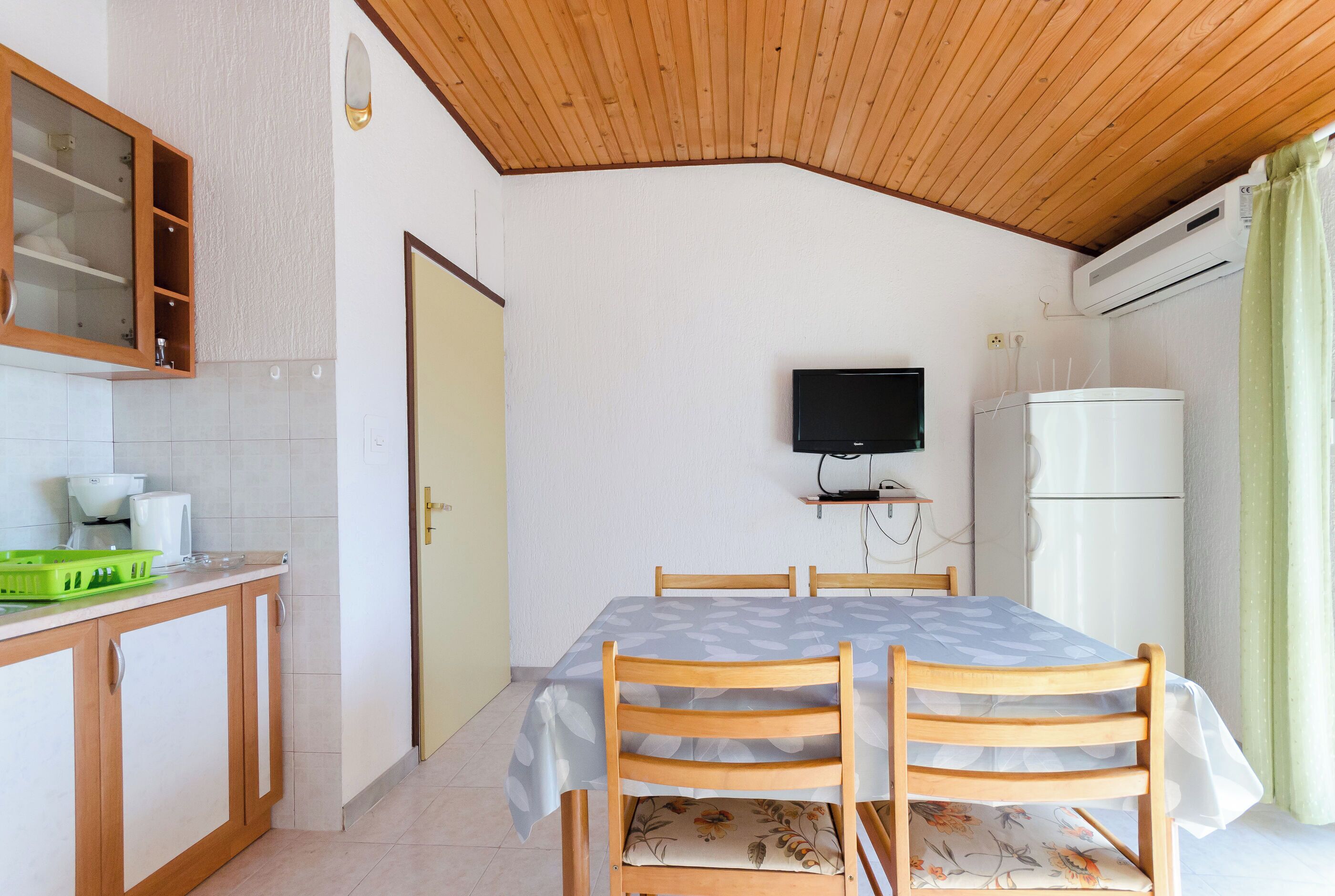 Una cocina compacta con comedor, techo de madera y televisor montado en la pared.