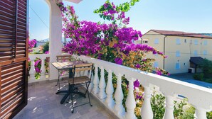 A balcony with a table and chairs, surrounded by white balustrades and purple flowers.