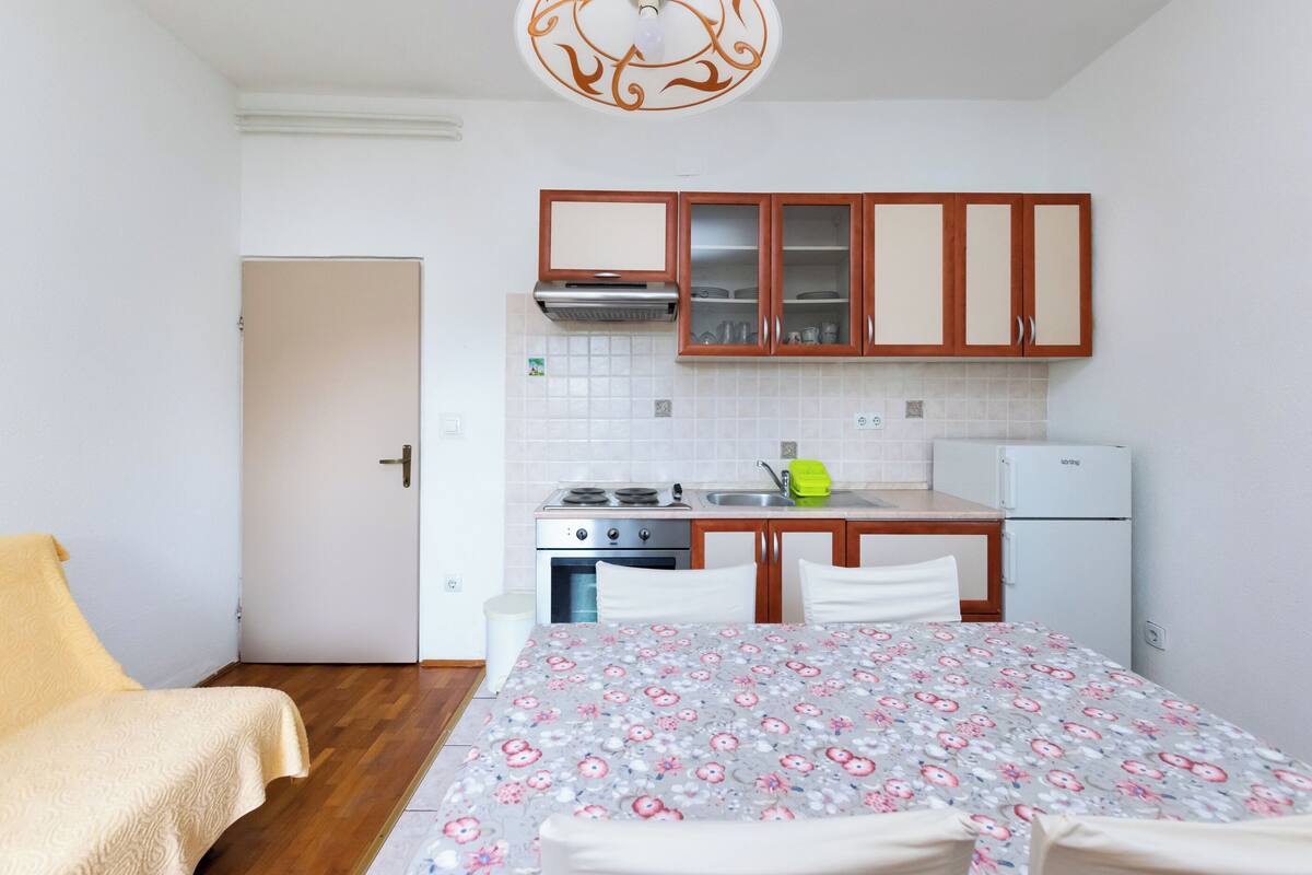 Une pièce de taille modeste comprenant un lit, un petit coin cuisine et une porte donnant sur une autre pièce.