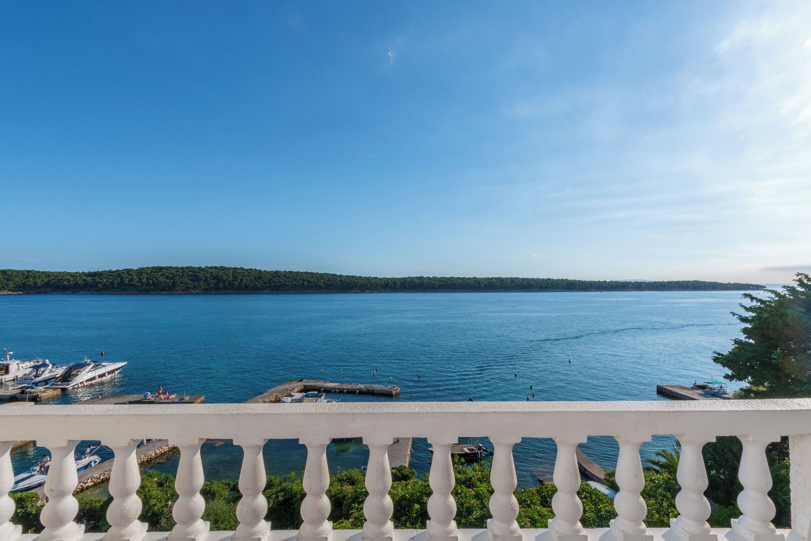 A waterfront view with boats docked, a pier, and a forested island in the distance.