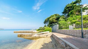 A coastal walkway with a stone wall, a boat, and a clear view of the sea. - Apartments Biserka (Rab)