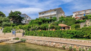 A coastal residential area with stone walls, a paved walkway, and buildings with balconies. - Apartments Biserka (Rab)