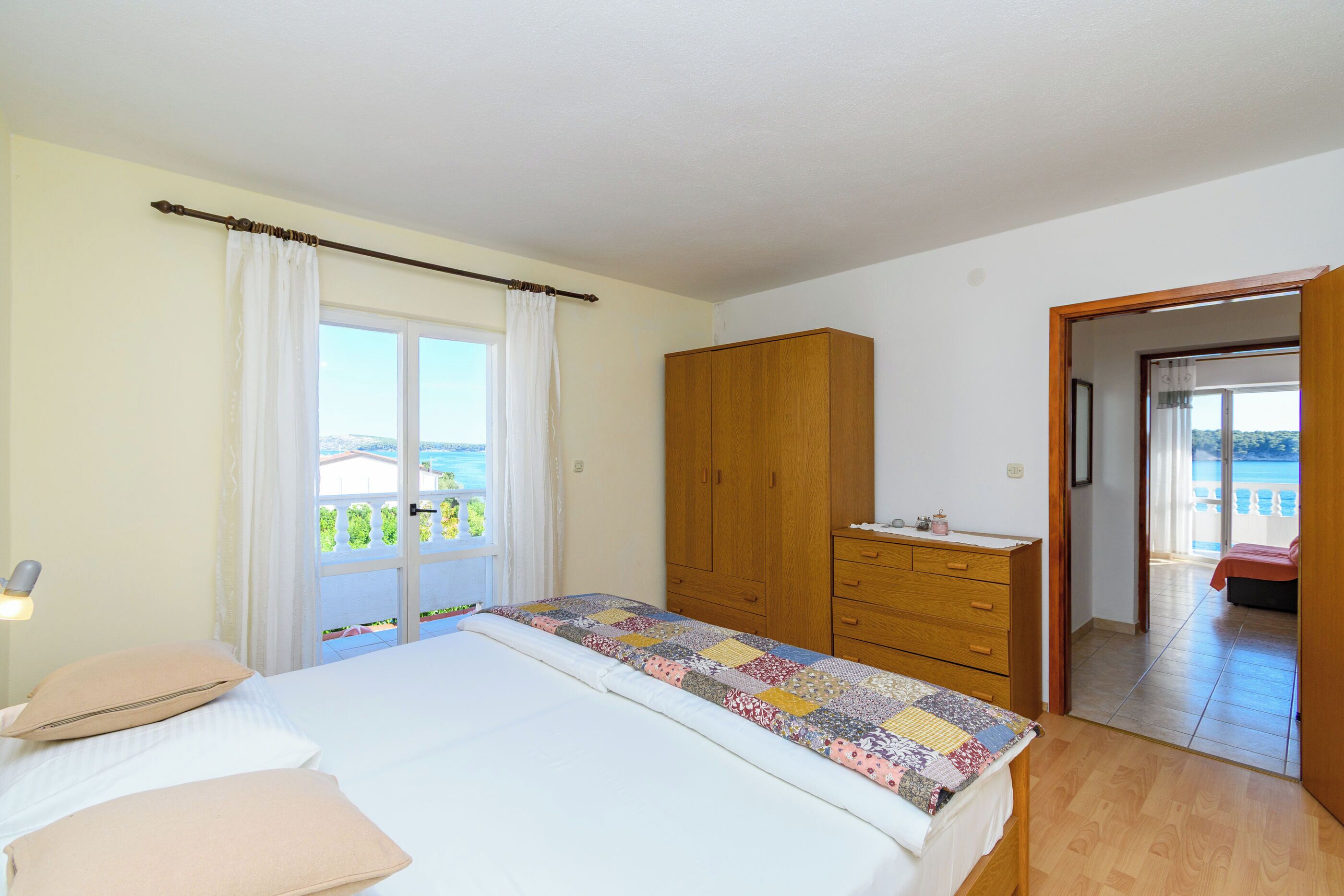 A bedroom with a bed, a wooden wardrobe, a window with curtains, and a view of the outside.