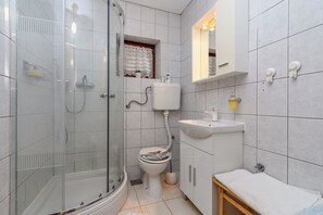 Un bagno con cabina doccia in vetro, un water, un lavandino e uno specchio sopra il lavandino.