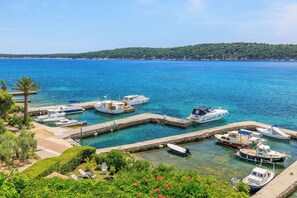Ein Yachthafen mit mehreren anglegerten Booten, umgeben von viel Grün und blauem Meer.