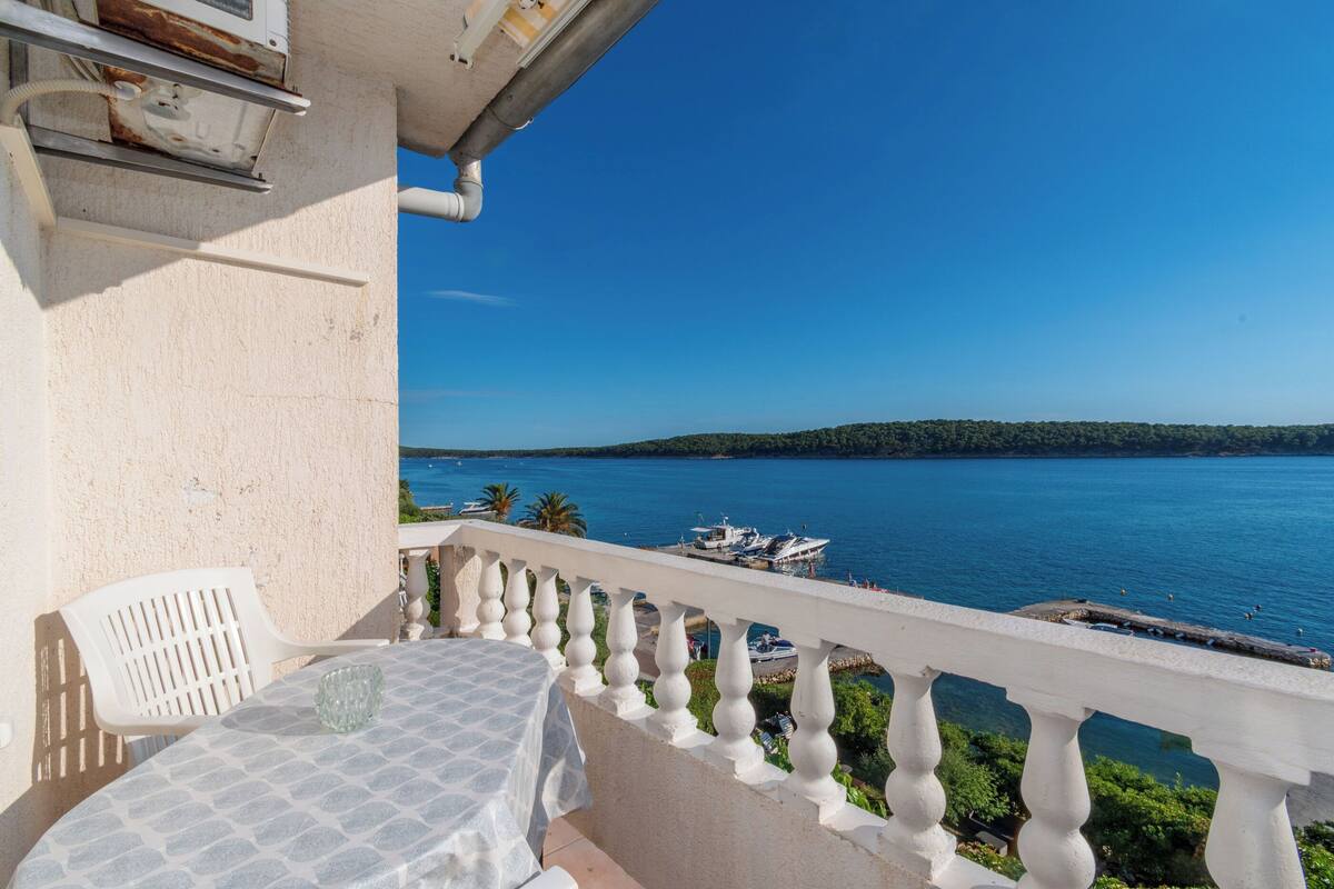 Un balcon avec une table et des chaises, donnant sur une étendue d’eau et sur une terre lointaine.