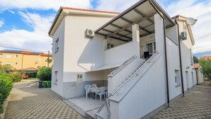 Un edificio de dos pisos con un espacio exterior cubierto, una escalera y un pequeño patio con sillas.