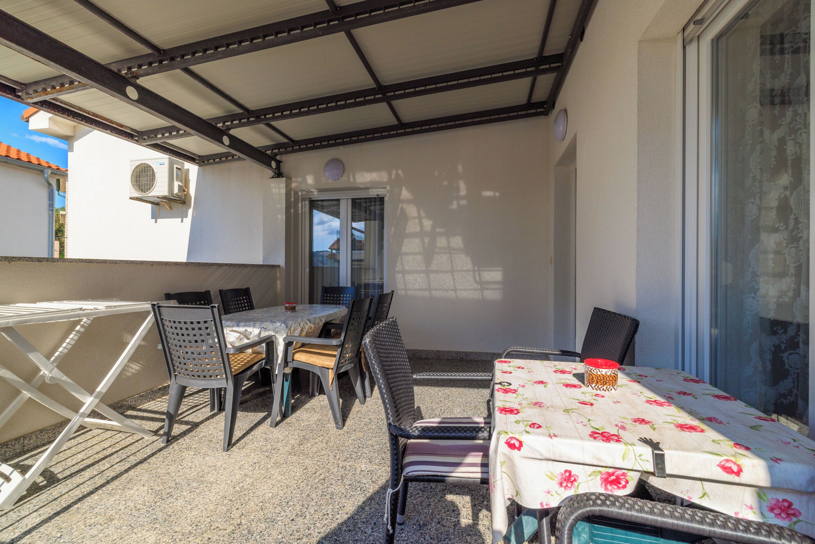 An outdoor patio with a table and chairs, a covered area, and a door leading to another room.