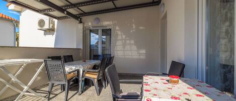 An outdoor patio with a table and chairs, a covered area, and a door leading to another room.