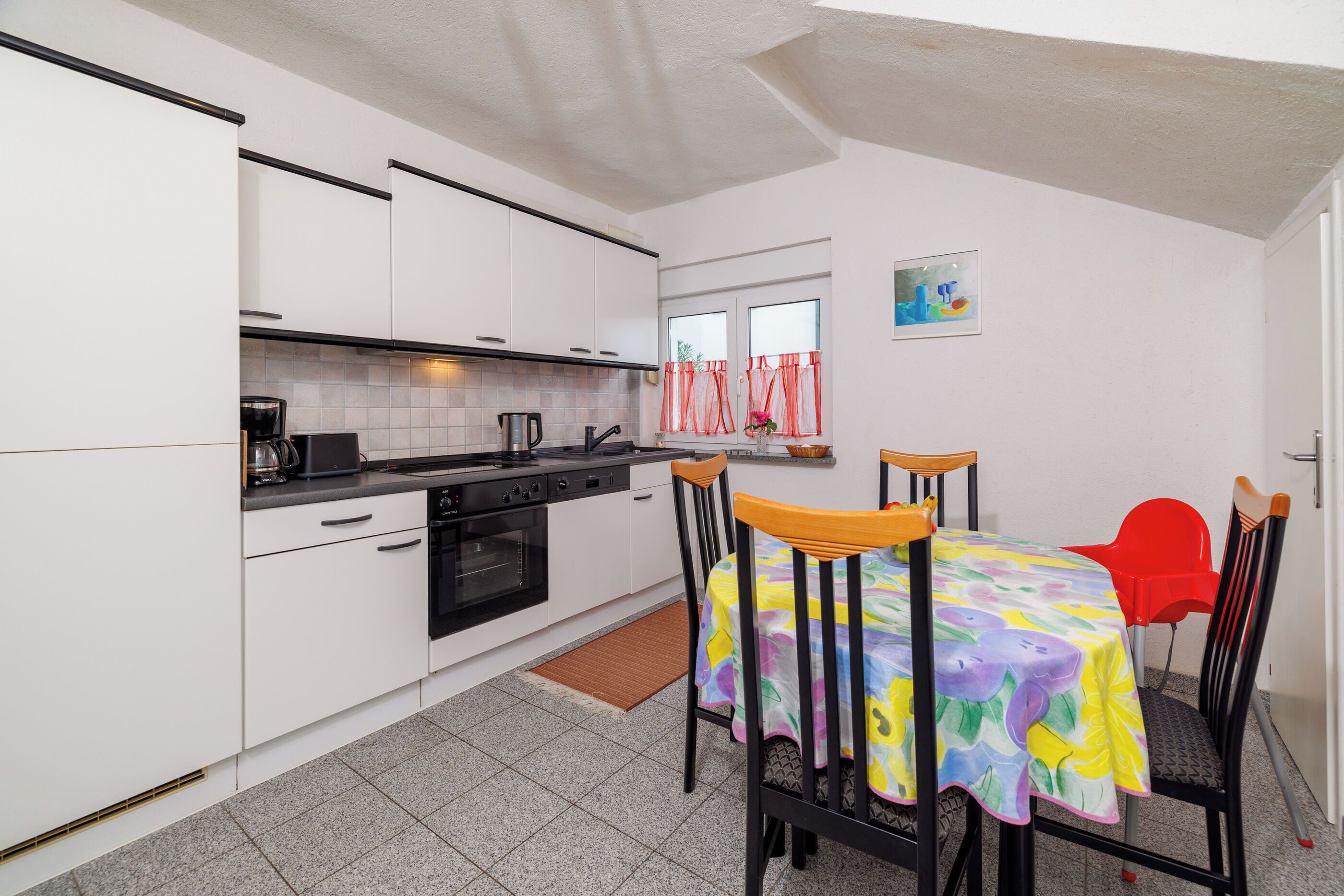A compact kitchen with white cabinets, a stove, and a dining area with a table covered in a colorful tablecloth.