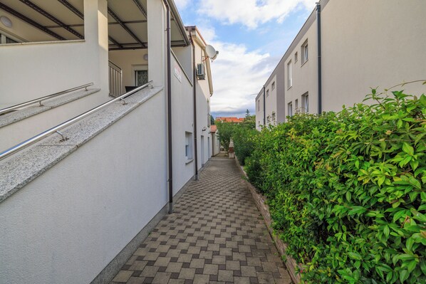 A narrow alleyway with a tiled walkway, bordered by white buildings and a hedge. - Apartments Stefica (Lopar)