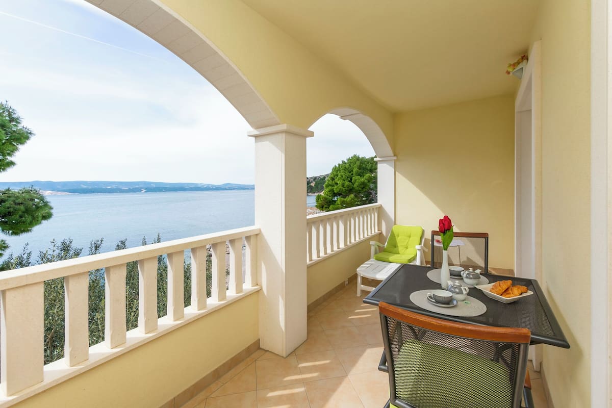 A balcony with a table set for breakfast, overlooking a body of water and greenery.