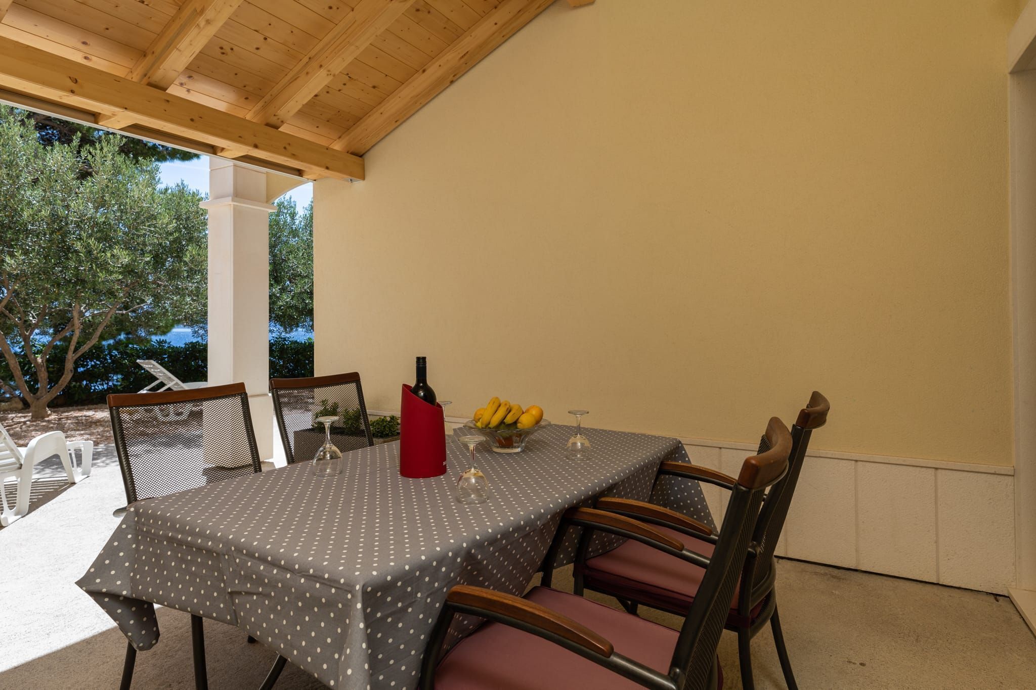 Un espace extérieur abrité, aménagé pour les repas, avec une table dressée pour quatre personnes, entourée de chaises.