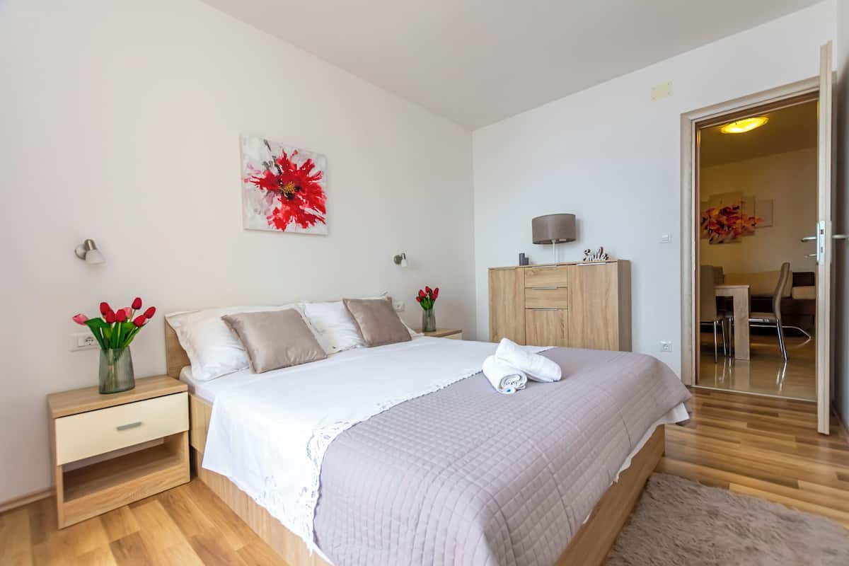A modern bedroom with a large bed, bedside tables, a wooden wardrobe, and a door leading to a bathroom.