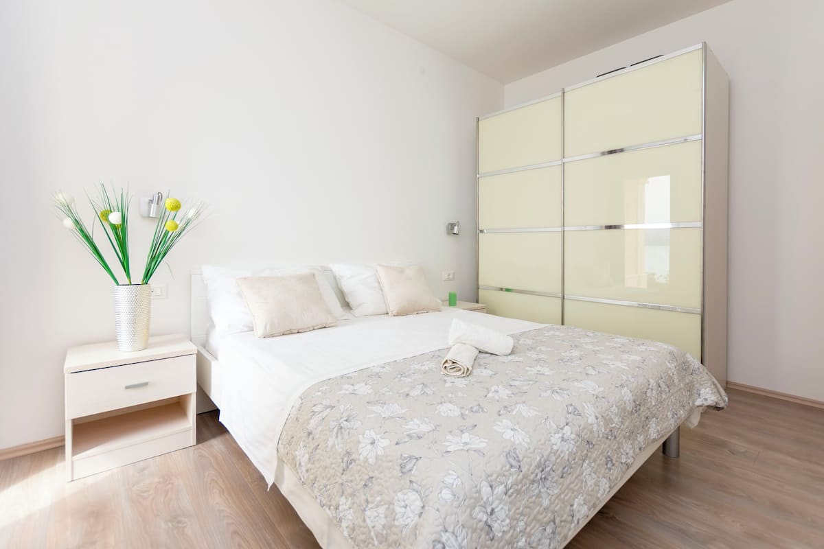 A bedroom with a bed, a nightstand, a bedside table, a wardrobe, and a vase with flowers.