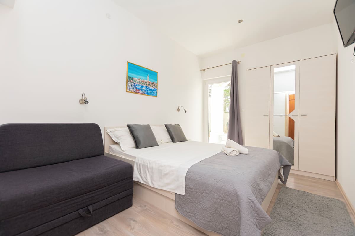 A bedroom with a bed, a sofa, a painting, and a wardrobe.