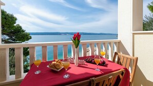 Un balcón con una mesa dispuesta para el desayuno, con vistas a un paisaje marino y colinas a lo lejos.