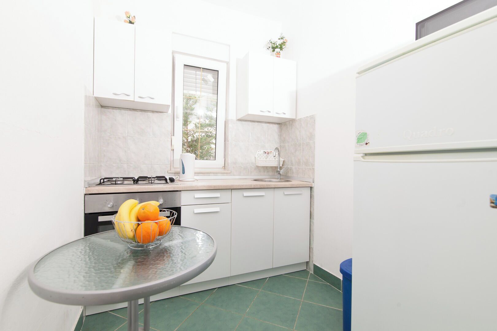 A compact kitchen with a gas stove, a sink, and a small table with a fruit bowl.