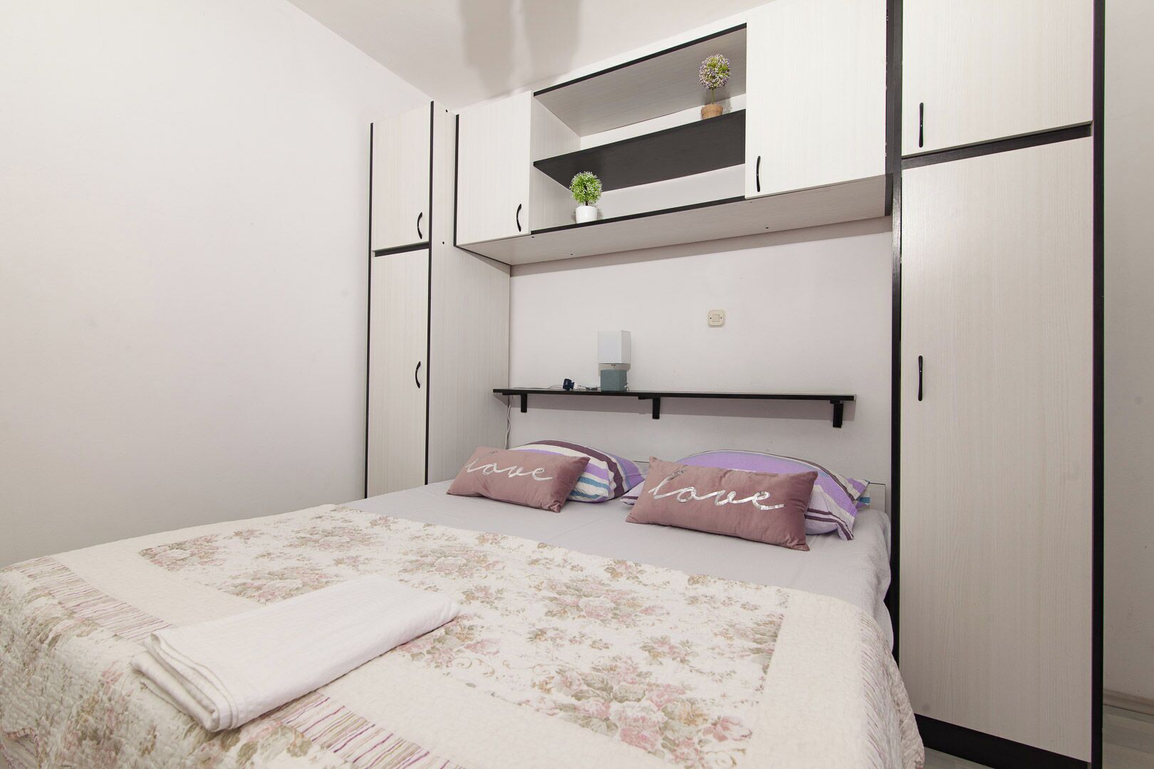 Une chambre à coucher comprenant un lit, une table de chevet, une étagère au-dessus du lit et une armoire.