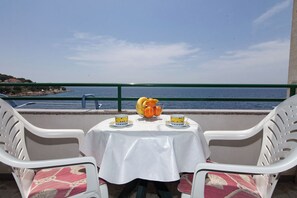 Uma mesa com toalha branca, duas cadeiras e uma fruteira com laranjas e bananas.