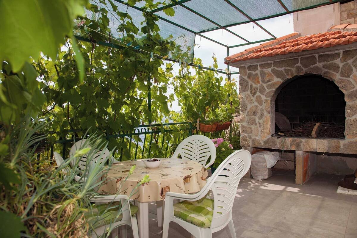 An outdoor patio with a stone oven, white plastic chairs, and a table with a bowl of food.