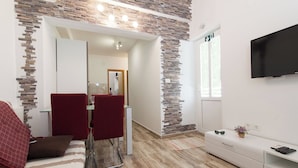A modern room with a stone accent wall, a TV mounted on the wall, a bed with a striped blanket, and a small table with a plant. - Apartments Gojka (Primosten)