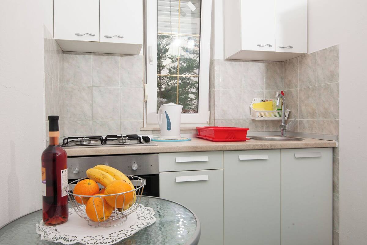 A kitchen with white cabinets, a gas stove, a sink, and a window with a view of trees.