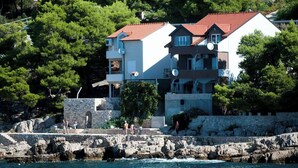 A coastal building with multiple balconies, a stone wall, and a view of the sea. - Apartments Gojka (Primosten)