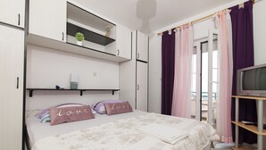 A bedroom with a bed, two shelves with plants, a TV, and a window with curtains. - Apartments Gojka (Primosten)