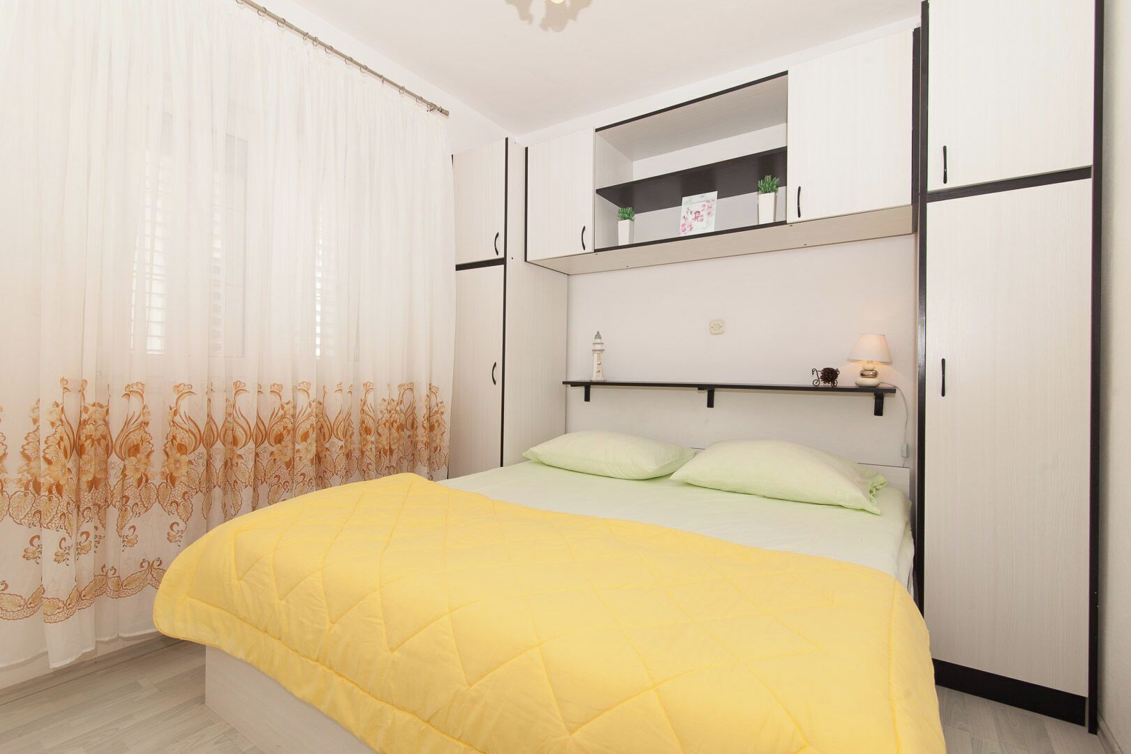 Una camera da letto con un letto, un armadio, uno scaffale con piante e un comodino con una lampada.
