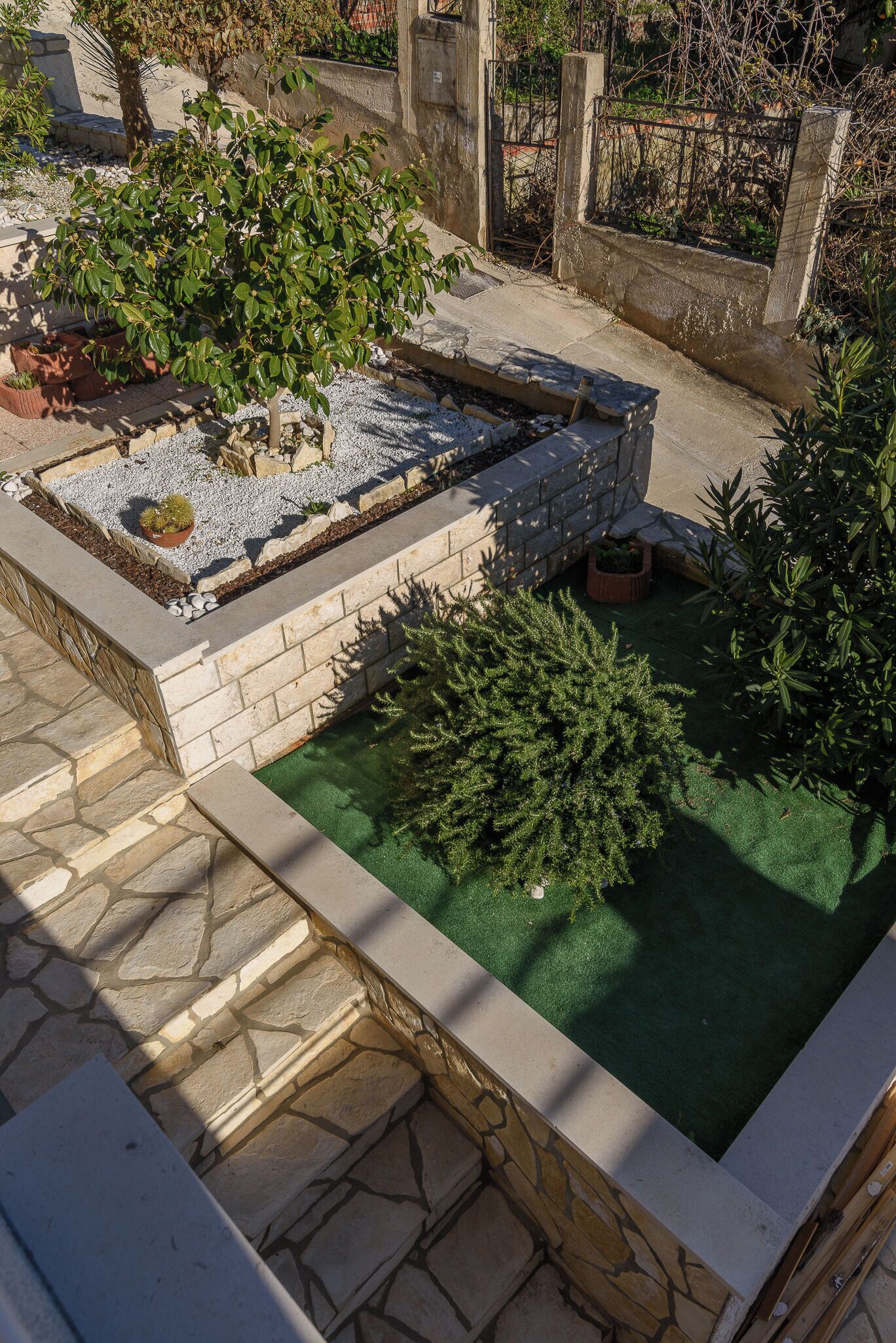 A rooftop garden with a small water feature, stone steps, and various plants.