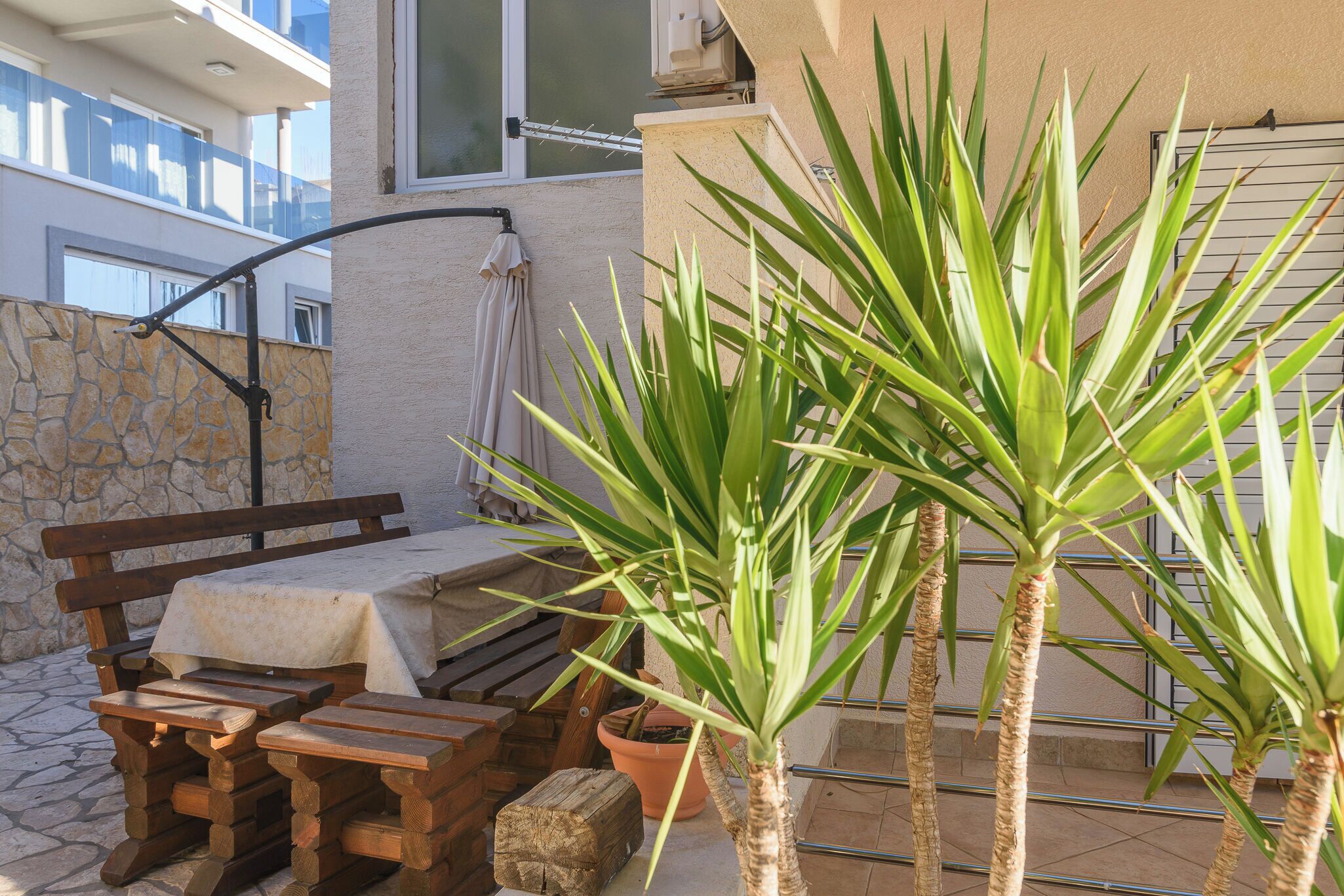 A patio with a wooden bench, a table, and a potted plant.