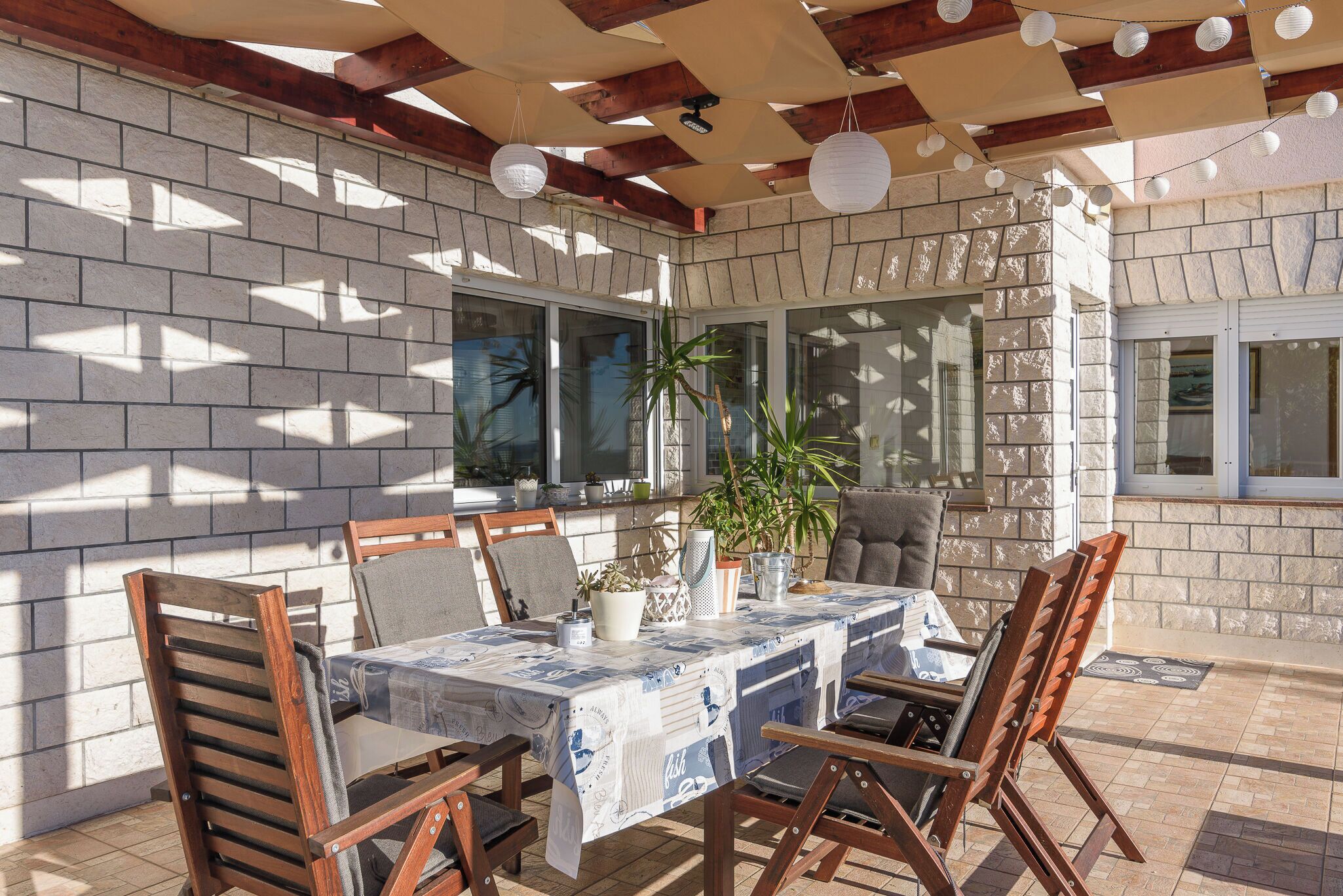 Un patio exterior con una mesa dispuesta para cuatro personas, rodeado de sillas de madera.
