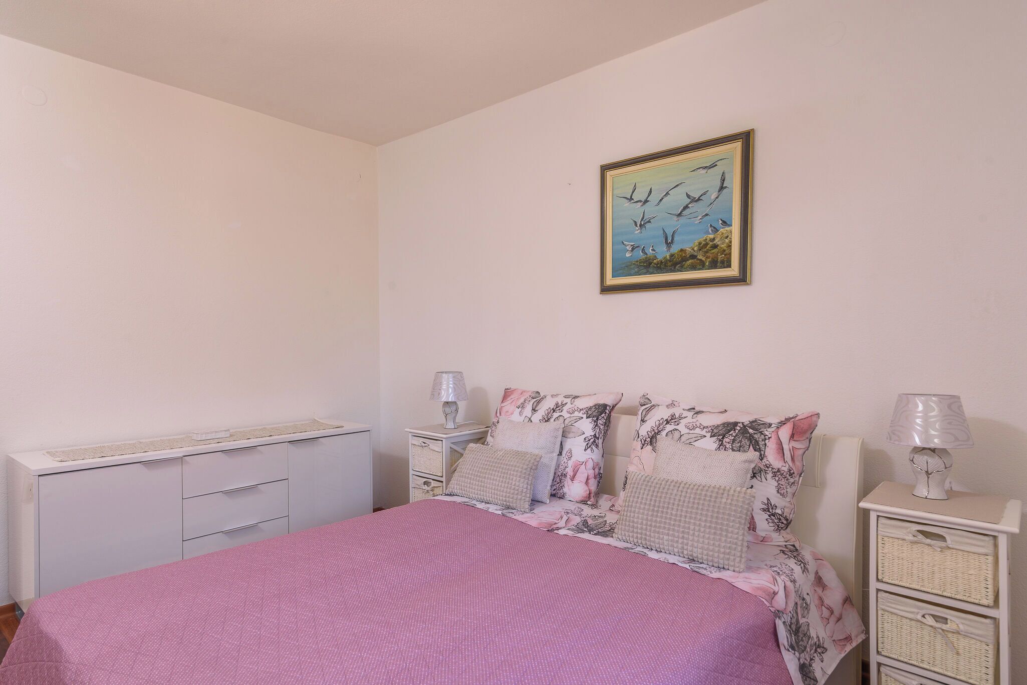 A bedroom with a bed, a nightstand, a dresser, and a wall-mounted painting.