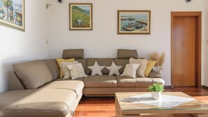 A living room with a beige sofa, a glass coffee table, and three framed landscape paintings on the wall. - Apartment Helli (Okrug)