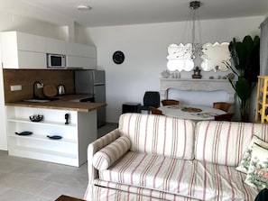A modern kitchen with white cabinets, a microwave, and a coffee machine. There is a striped sofa and a dining table with chairs. - Apartments Livingston (Novi Vinodolski)
